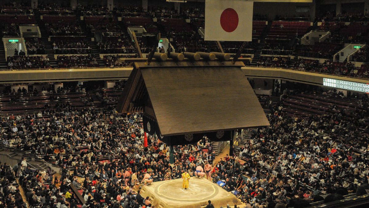 Large crowd watches a traditional sumo wrestling match inside a Japanese arena.