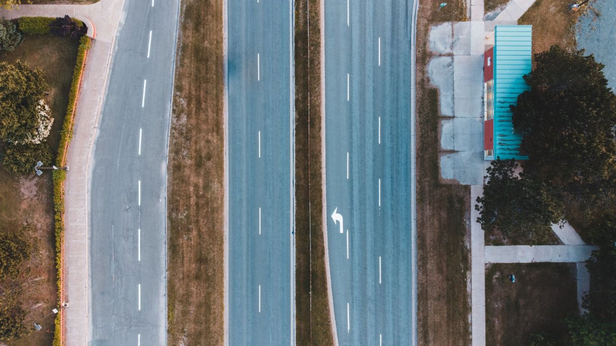 Bird's eye view of an empty urban two-lane highway with adjacent bus stop and greenery.