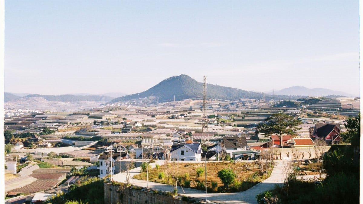 Expansive rural landscape with fields and hills under a clear sky, seen from a hilltop.