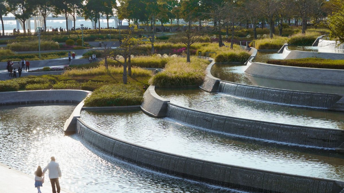 A serene park landscape with cascading water features and walking paths.
