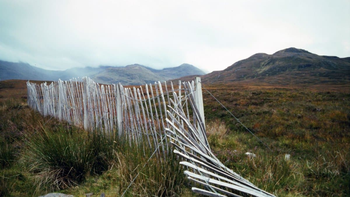 Rural landscape in the Scottish Highlands featuring a rustic white wooden fence and rolling hills.