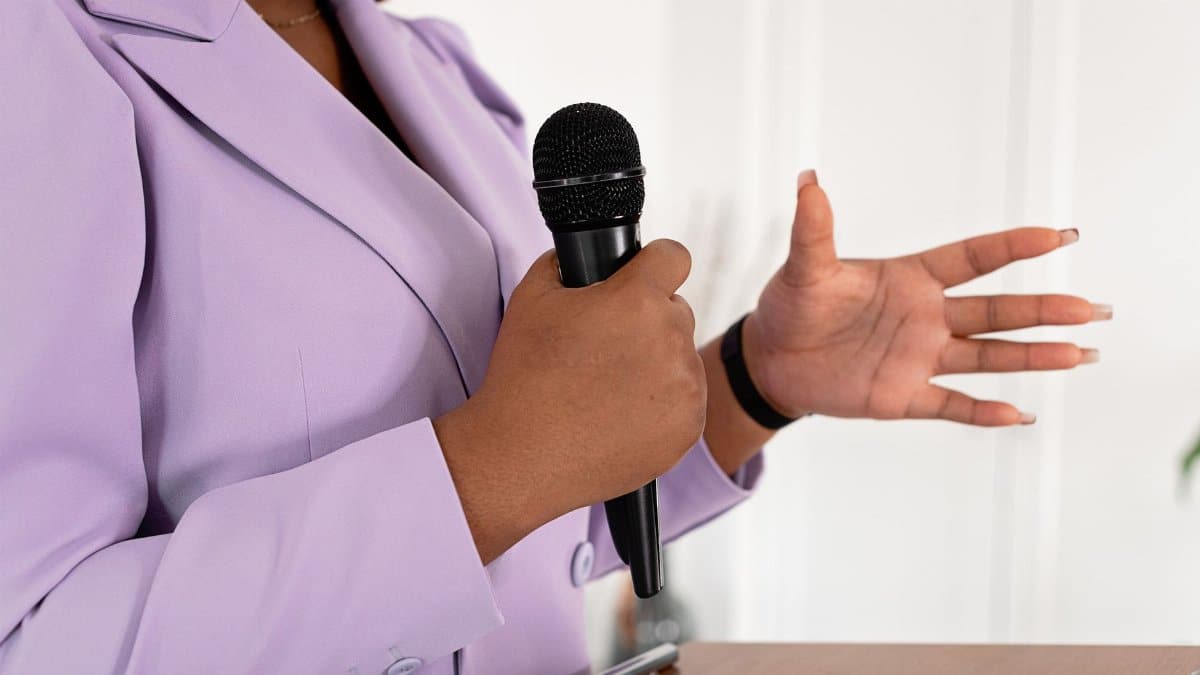 Close-up of a professional woman speaking with a microphone while gesturing.