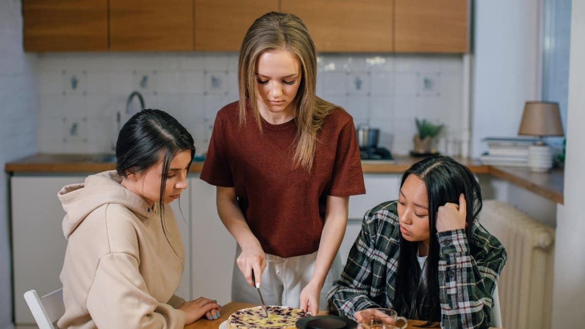 Three young women engaged in baking a pie in a cozy kitchen environment, conveying companionship.