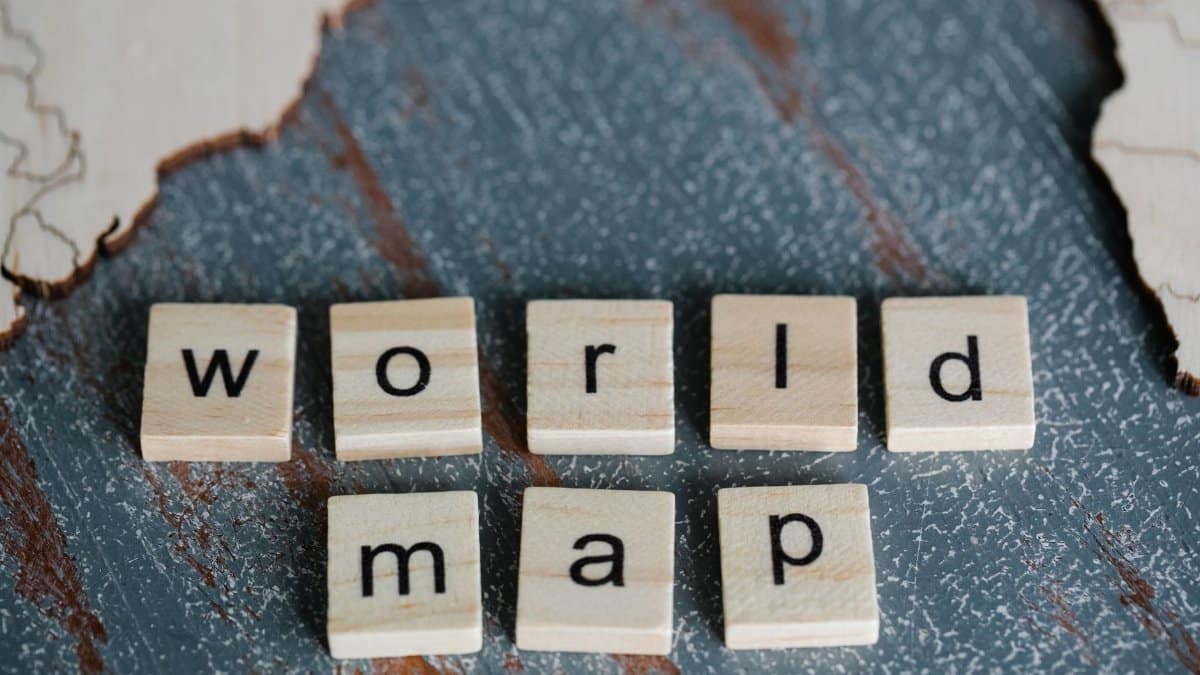 Close-up of Scrabble tiles spelling 'world map' on a textured wooden surface with map outlines.