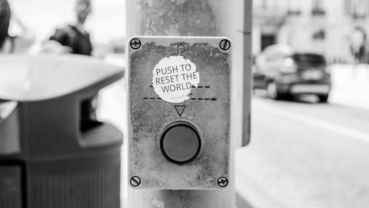Grayscale photo of a street button labeled 'Push to reset the world', Lisbon urban scene.