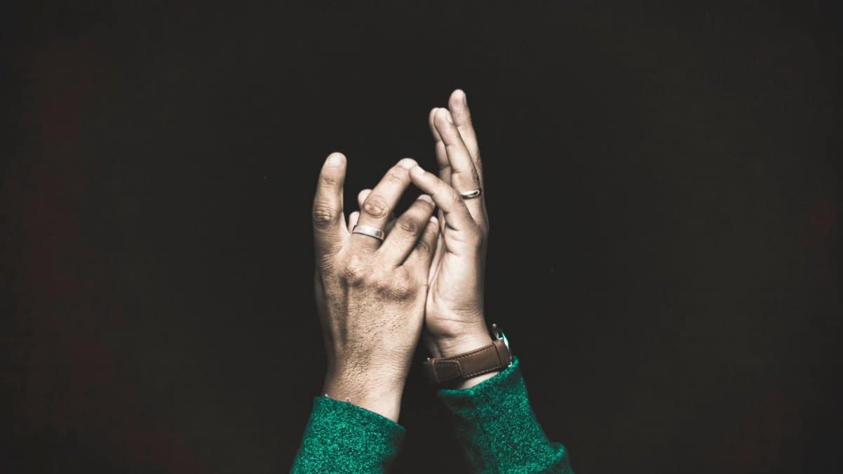 Close-up of hands clapping on a dark background, with visible rings and wristwatch.