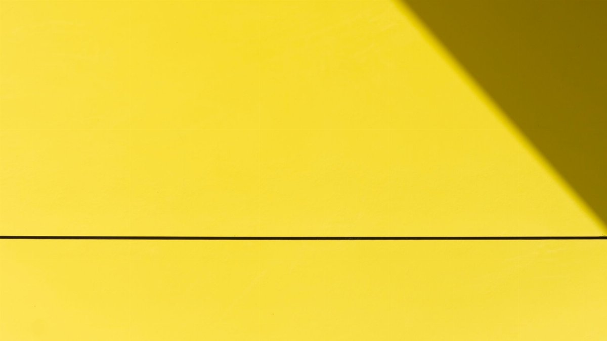 Minimalistic image of a bright yellow wall with a shadow creating a diagonal line.