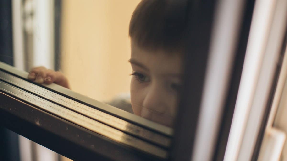 A child gazes pensively through a window, capturing a moment of curiosity and introspection.