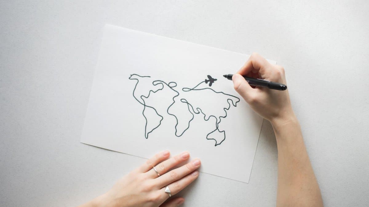 Hands drawing world map on paper, representing travel and creativity concepts.