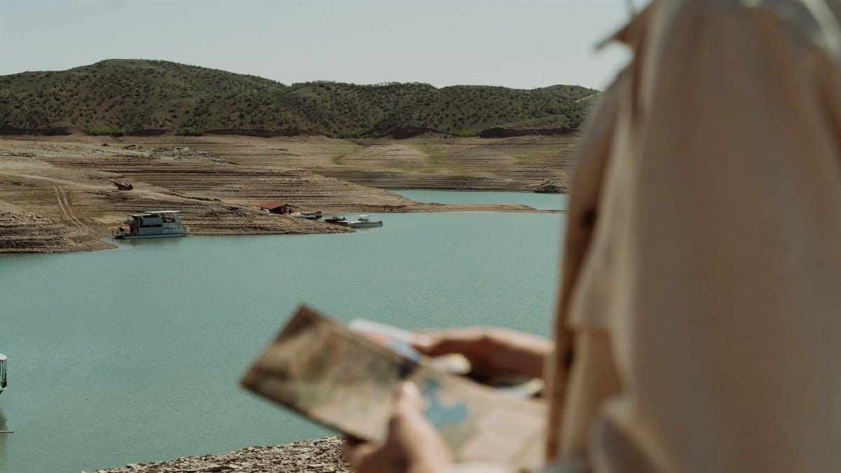 Traveler studies map by tranquil lake surrounded by hills.