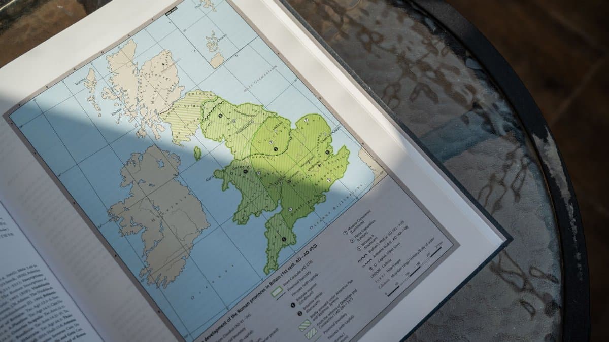A detailed map of Roman Britain in an open book on a glass table.