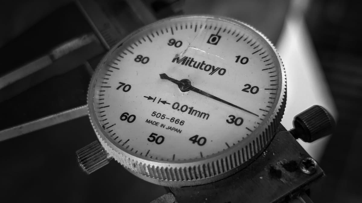 Detailed black and white image of a Mitutoyo dial indicator measuring tool, showcasing precision engineering.