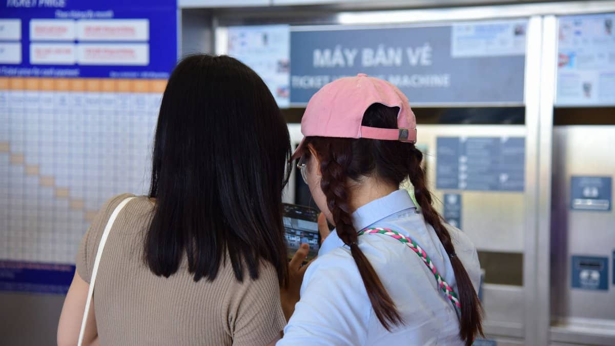 Two women purchasing tickets from a vending machine at a public transport station.