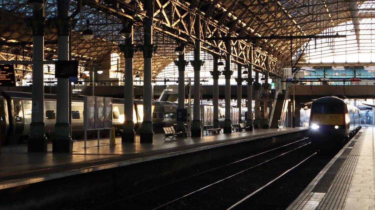A train arrives at Manchester Piccadilly Station as early morning light streams through the roof.