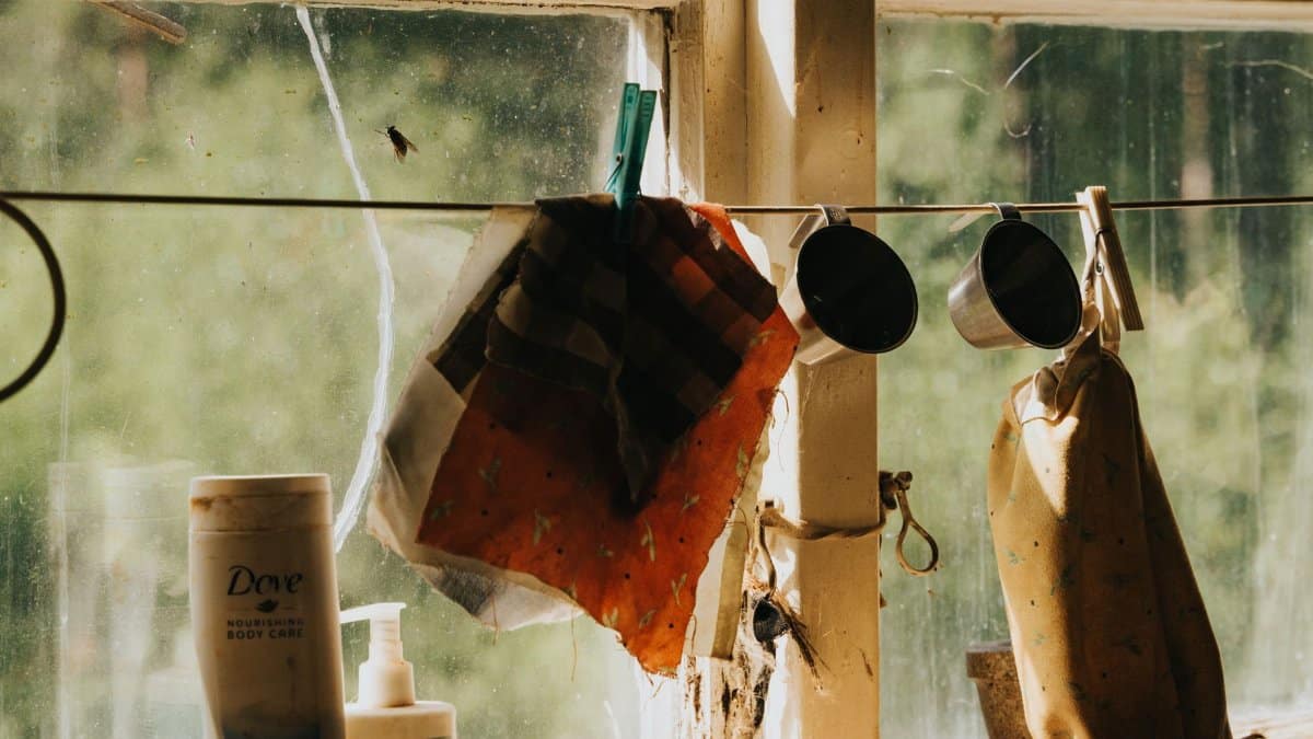 A nostalgic look at a sunlit window featuring hanging cloths and cups for a rustic vibe.