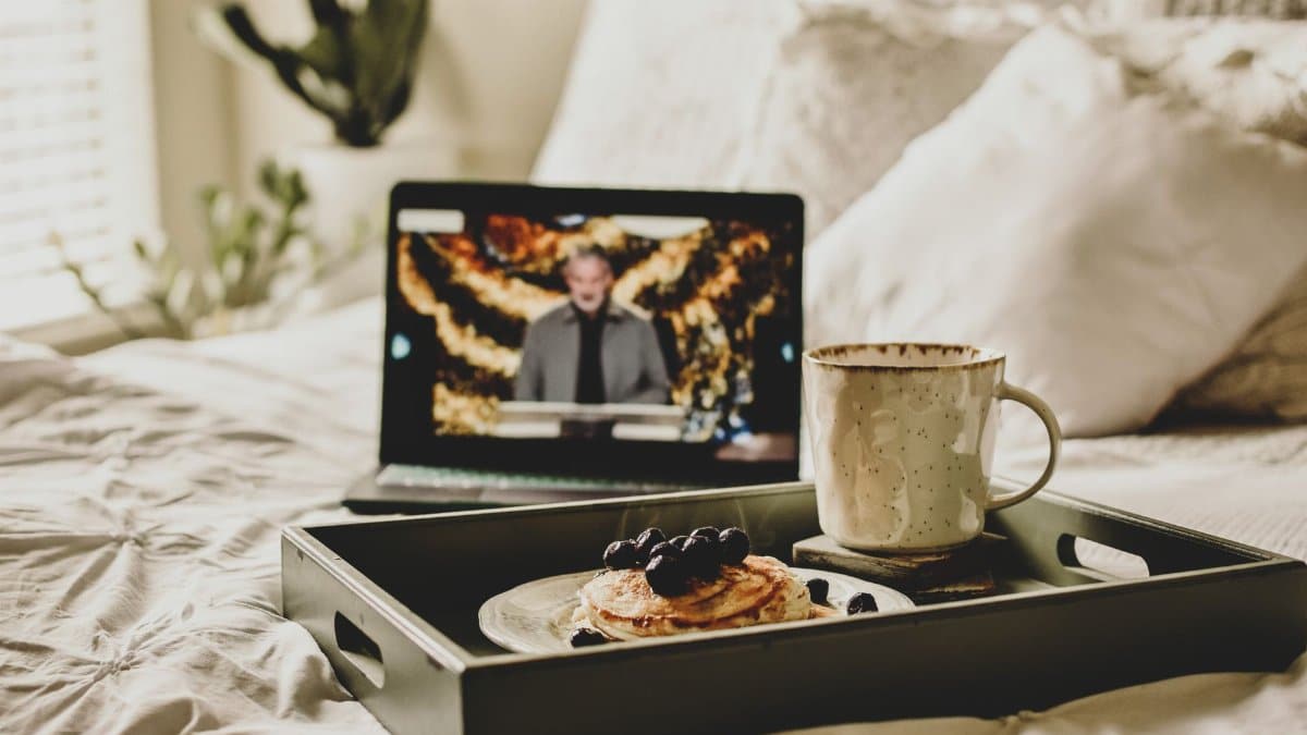 Enjoy a cozy morning in bed with pancakes, coffee, and online streaming entertainment nearby.