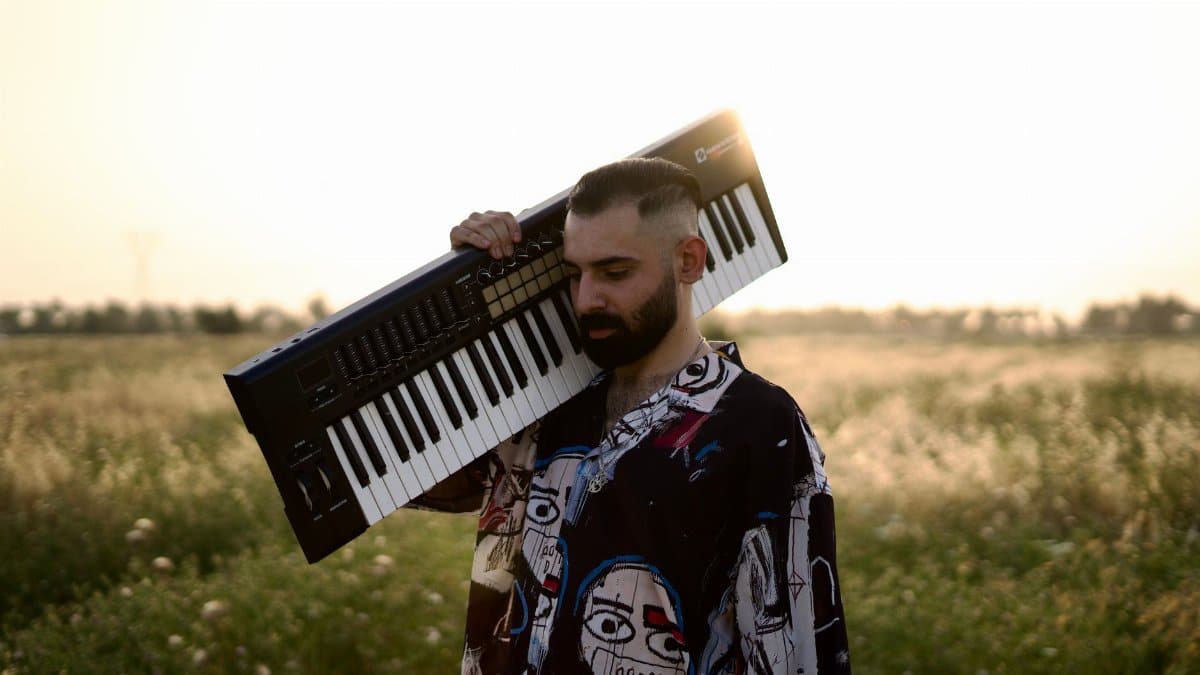 A musician carries a keyboard in a sunlit field in Baghdad, embracing a serene, artistic moment.