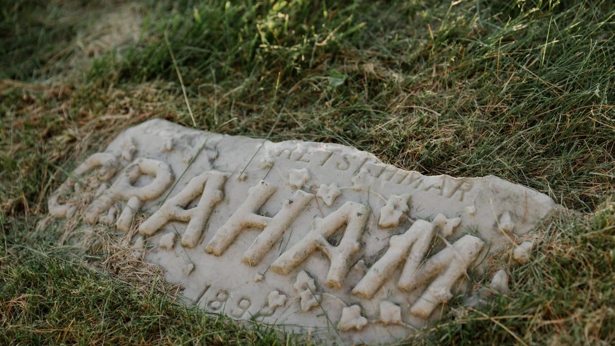 Close-up of a worn gravestone partially covered by grass, displaying 'Graham.'