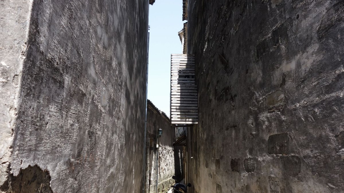A narrow alleyway with textured walls and dramatic lighting, showcasing urban architecture.