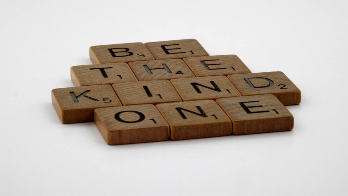Wooden Scrabble tiles spelling 'Be The Kind One' with focus on words and white background.