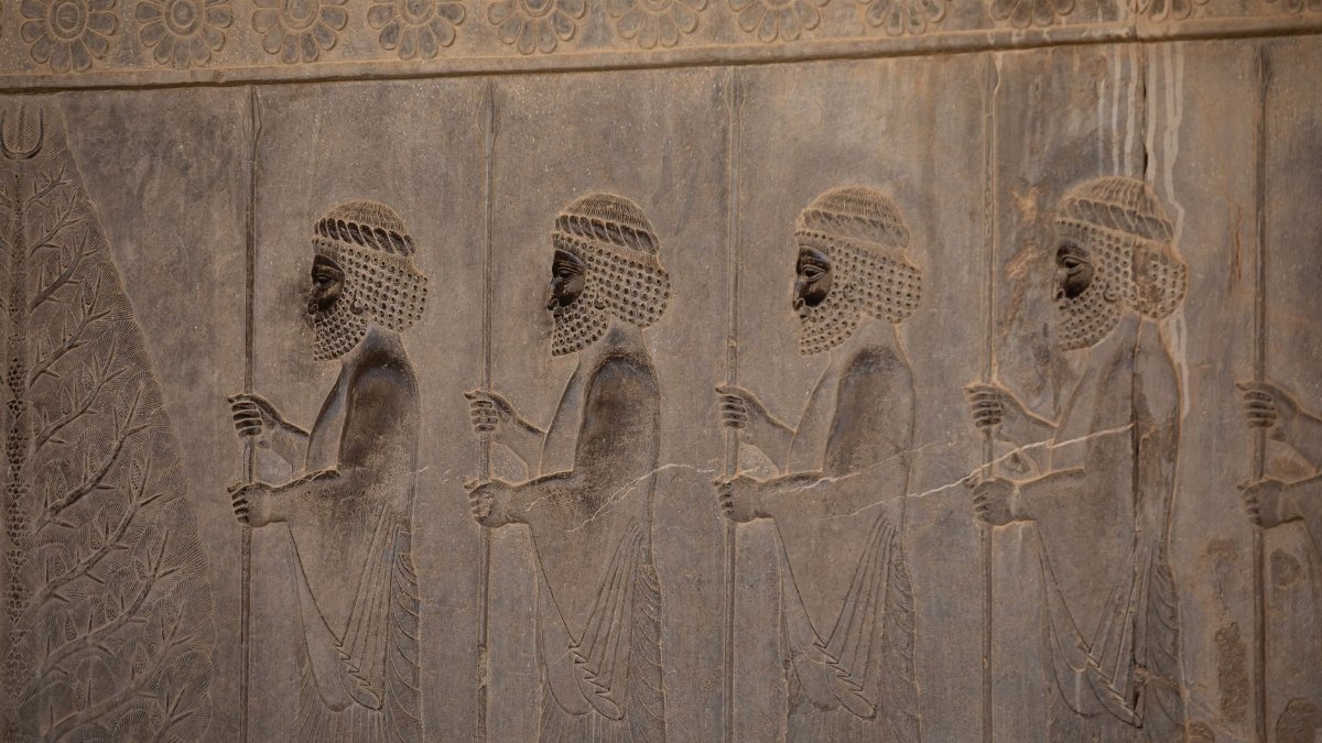 Intricate ancient Persian relief with figures in traditional attire carved into stone.