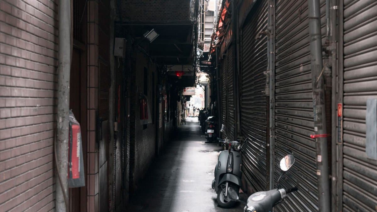Urban alleyway in Taipei featuring parked scooters and closed shutters.