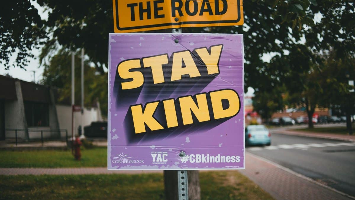 Close-up of a sign with 'Stay Kind' message on a city street.