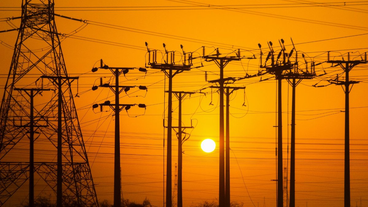 Silhouette of electric towers during sunset, highlighting power lines with a warm orange sky.