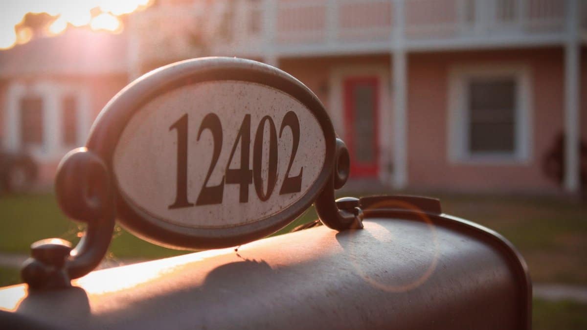 A vintage-style mailbox with the morning sun illuminating a house in the background.
