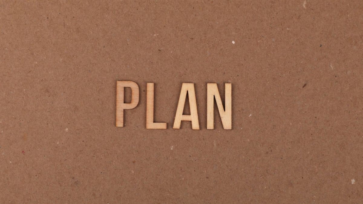 Wooden letters spelling 'PLAN' on a textured cardboard background with ample copy space.