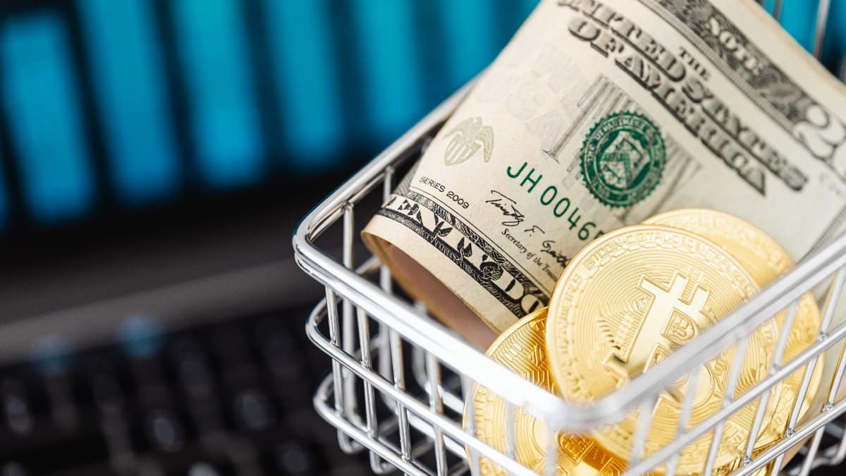 Close-up of bitcoin coins and US dollars in a shopping cart on a laptop, symbolizing digital finance.