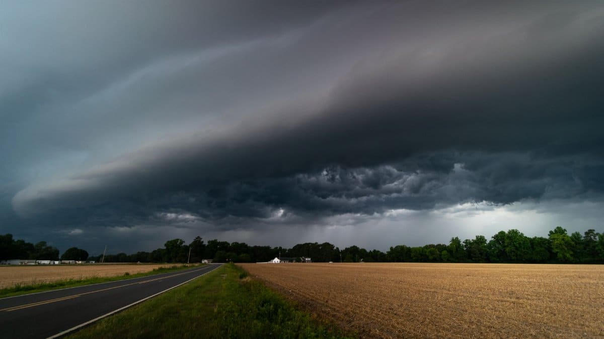 A mesmerizing view of dark storm clouds approaching over a rural road and farmland.