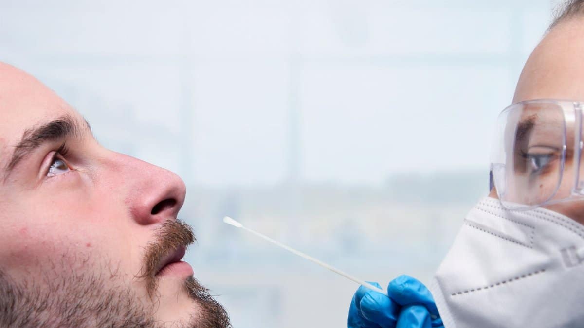 Healthcare worker administering a nasal swab test for COVID-19 detection indoors.