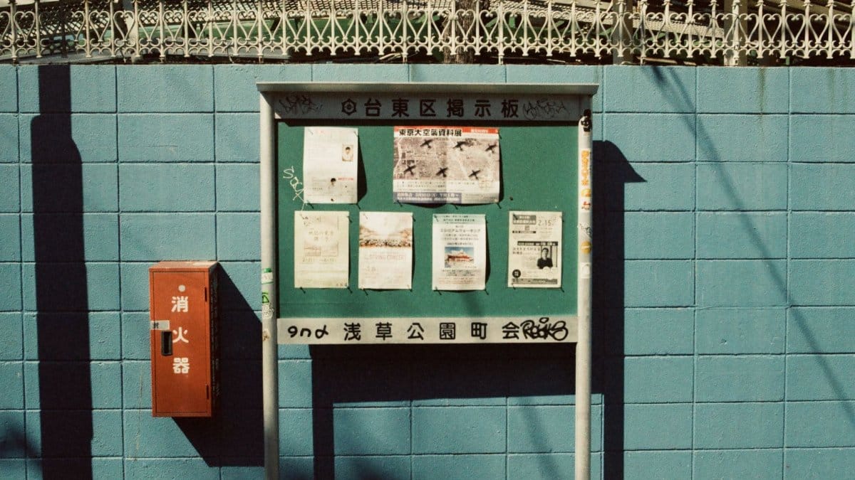 A vintage notice board with posted papers against a blue brick wall in Tokyo, Japan.