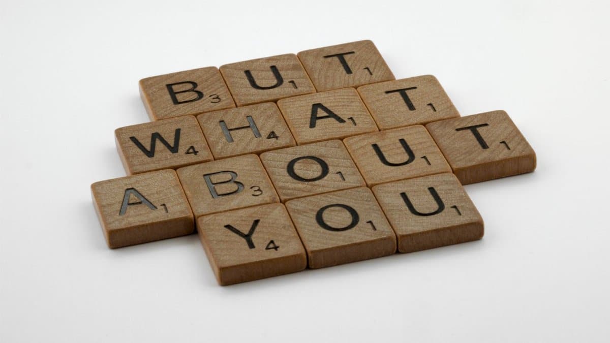Close-up of wooden Scrabble tiles spelling 'But What About You' on a white surface.