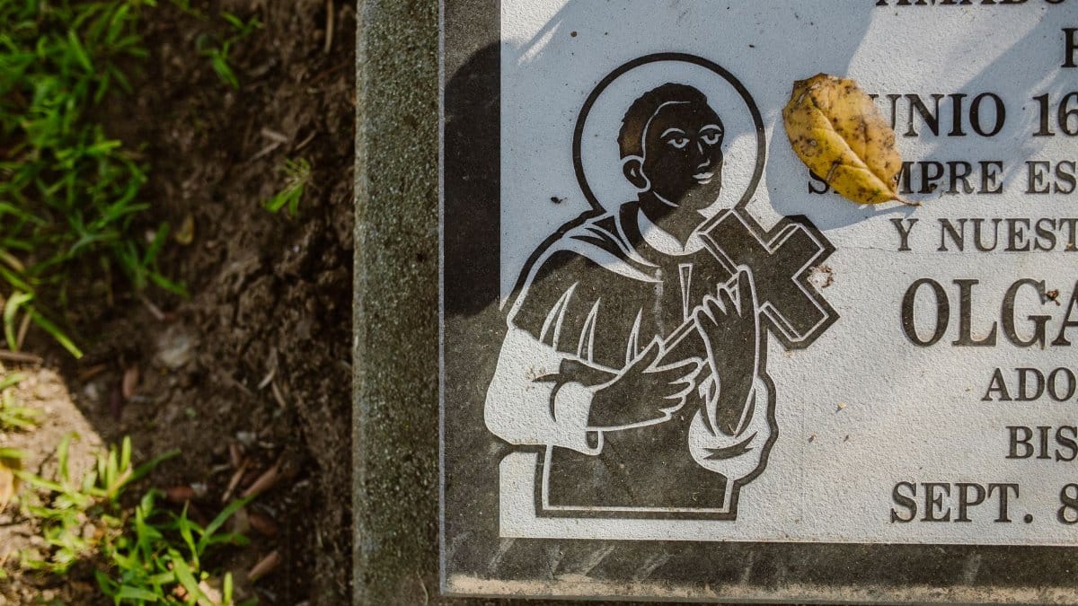 Detailed view of a gravestone featuring a religious icon and a fallen leaf.