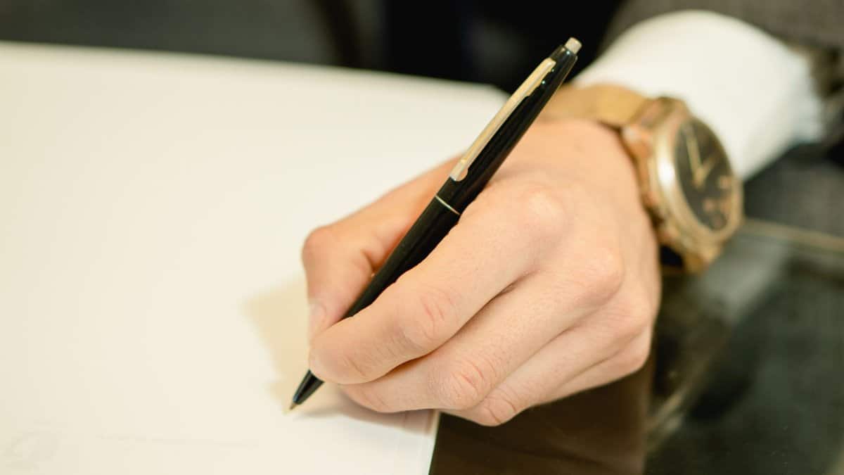 A close-up image of a hand holding a pen and writing on white paper, symbolizing business and communication.