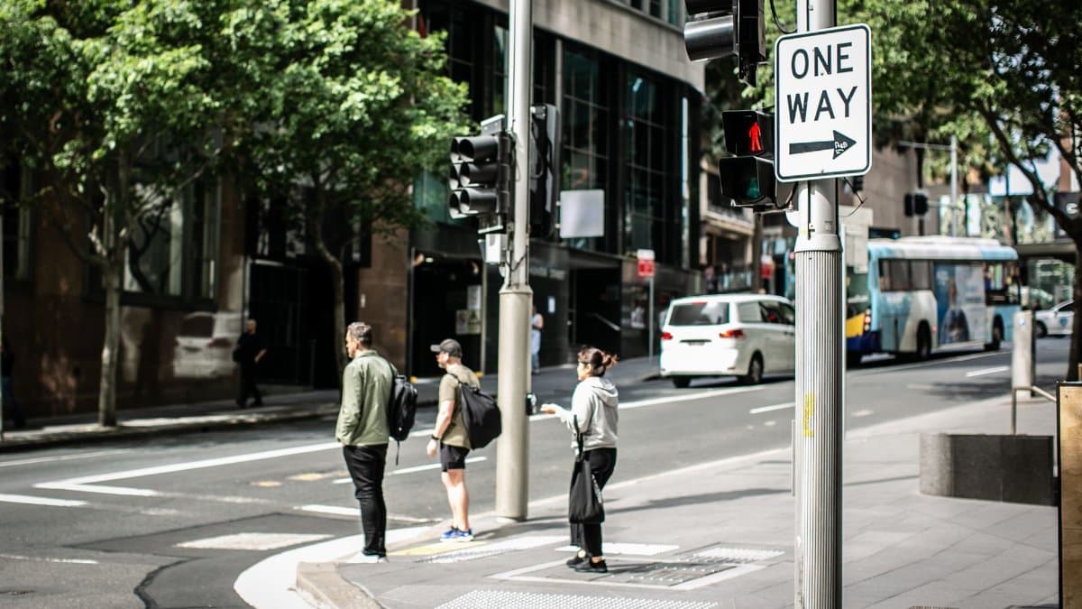 People waiting at a crosswalk on a sunny day in Alexandria, New South Wales with prominent one-way signage.