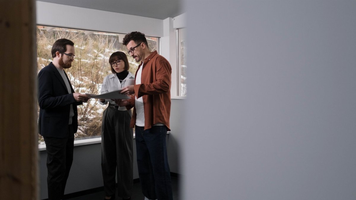 Three adults discussing a project inside a well-lit modern office setting.