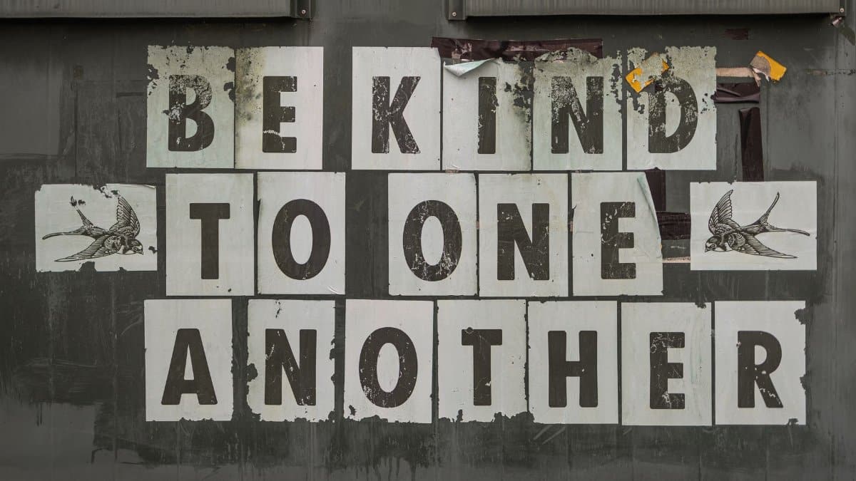 Close-up of 'Be Kind to One Another' message on a weathered background.