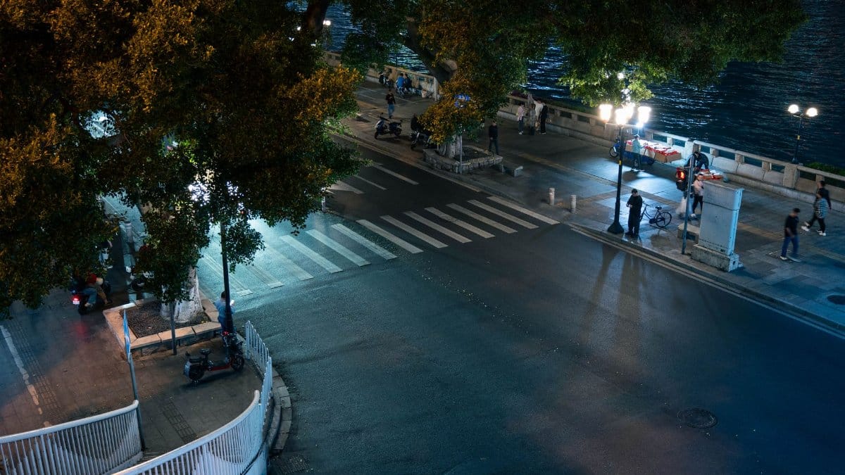 Aerial view of an illuminated city street and riverside at night with people walking.