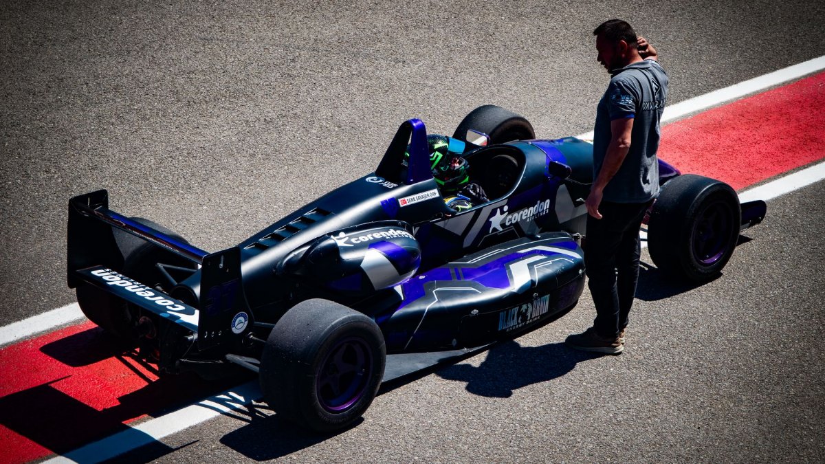 A Formula One race car on the track with a driver and pit crew member during the day.