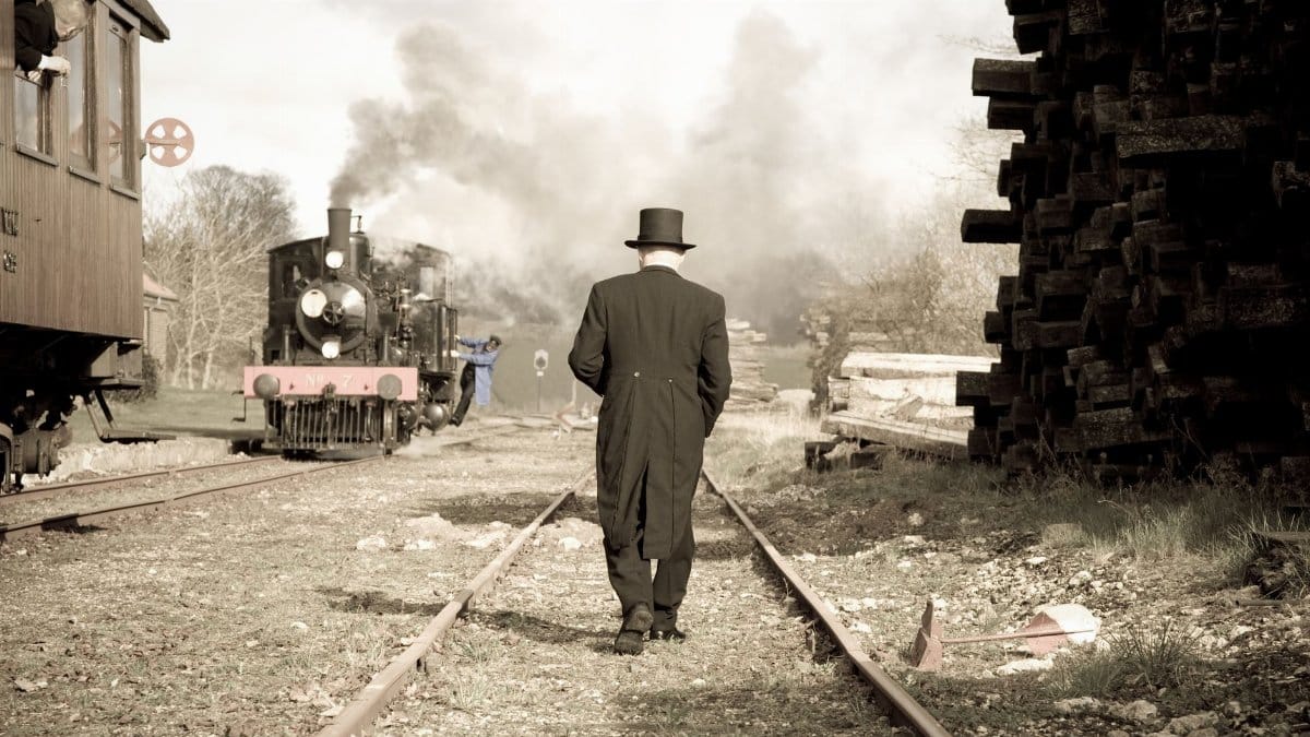 Retro scene of a man in a suit walking along a railroad with a steam train.