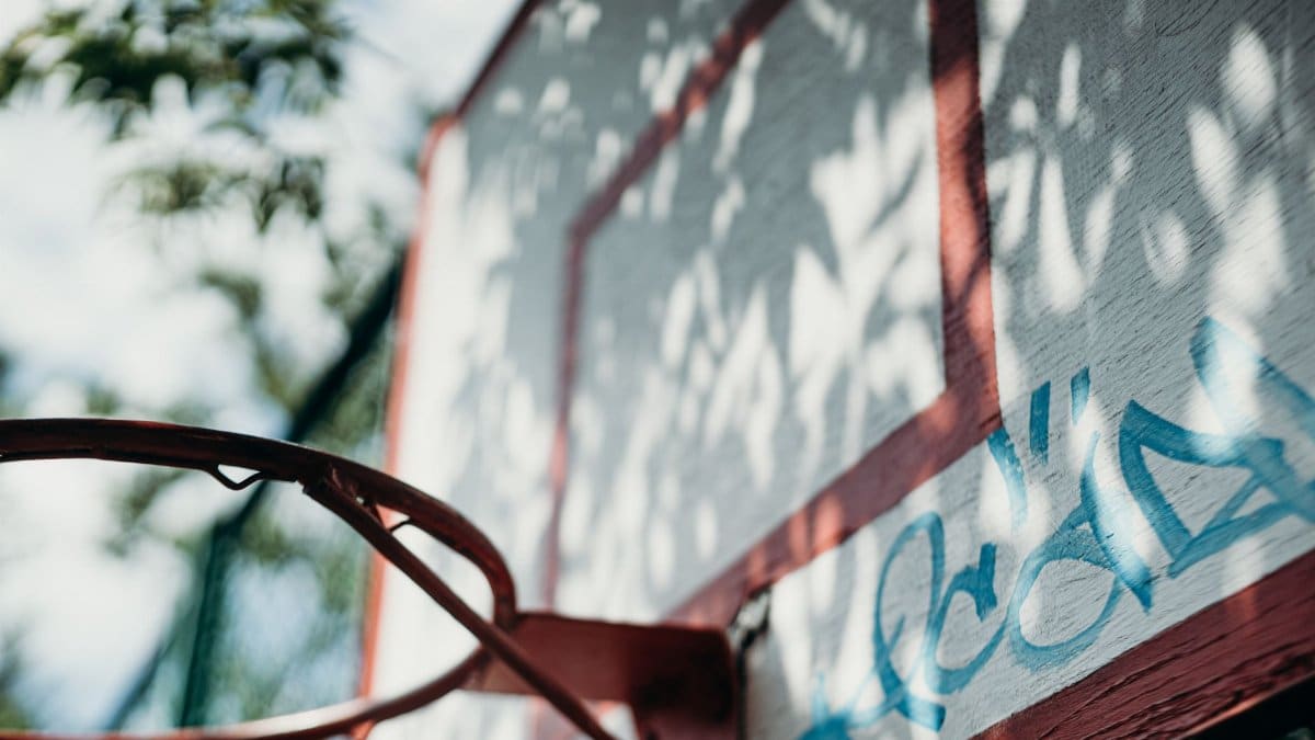 An artistic close-up of a basketball hoop and backboard with graffiti.