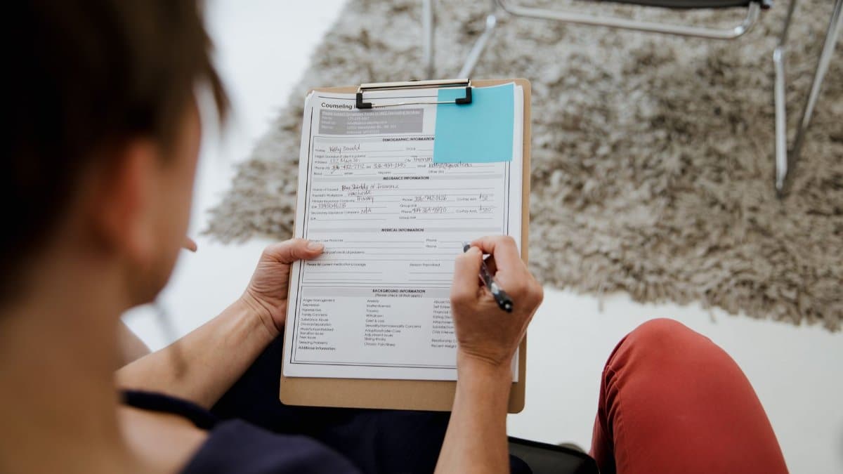 An adult woman writing on a counseling form during a business appointment in an office setting.