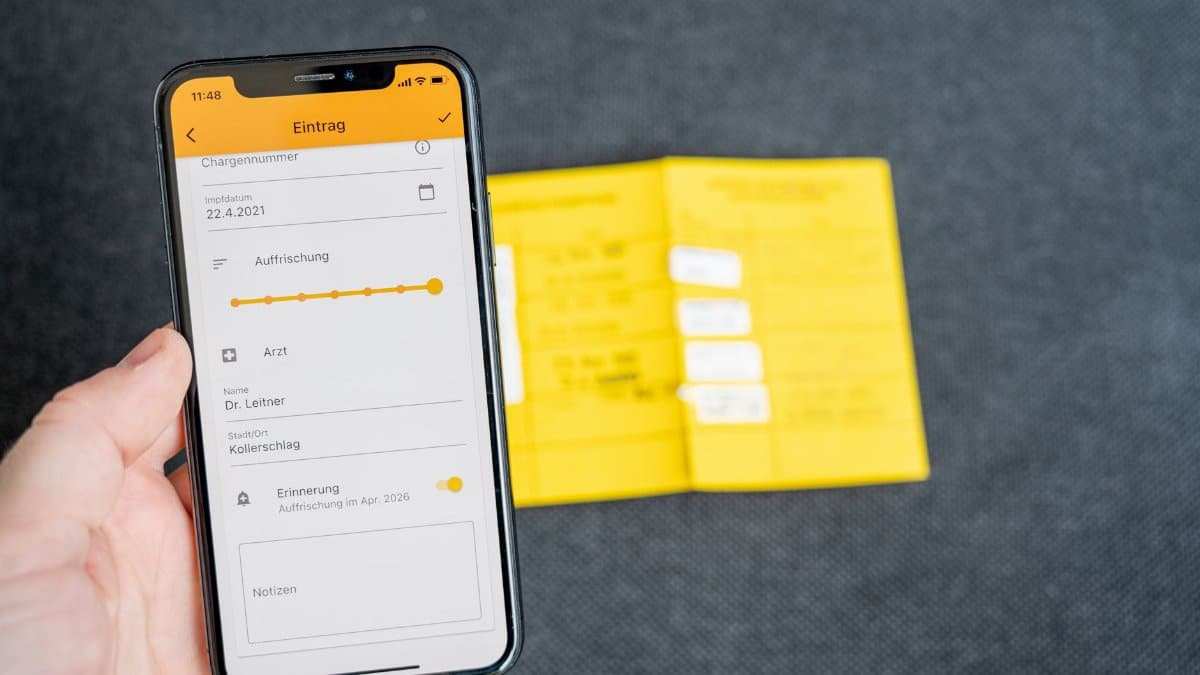 Close-up of a smartphone displaying a health record app held in hand with vaccine card visible.