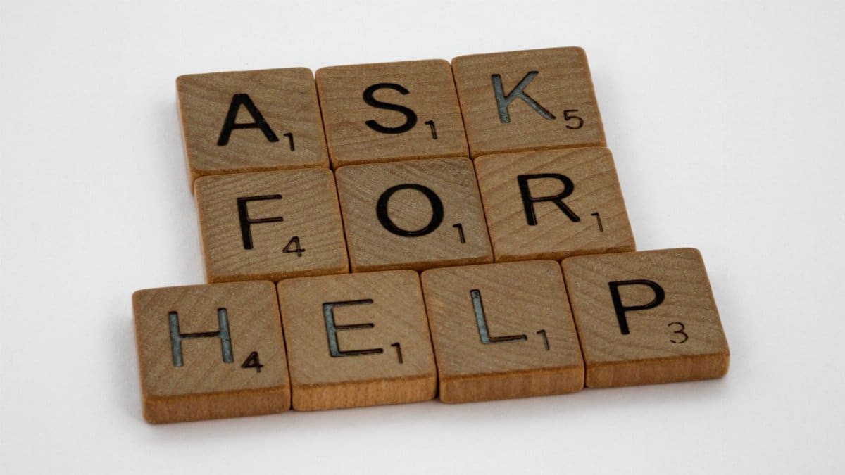 Wooden Scrabble tiles on a white surface spelling 'Ask for Help' in a conceptual layout.