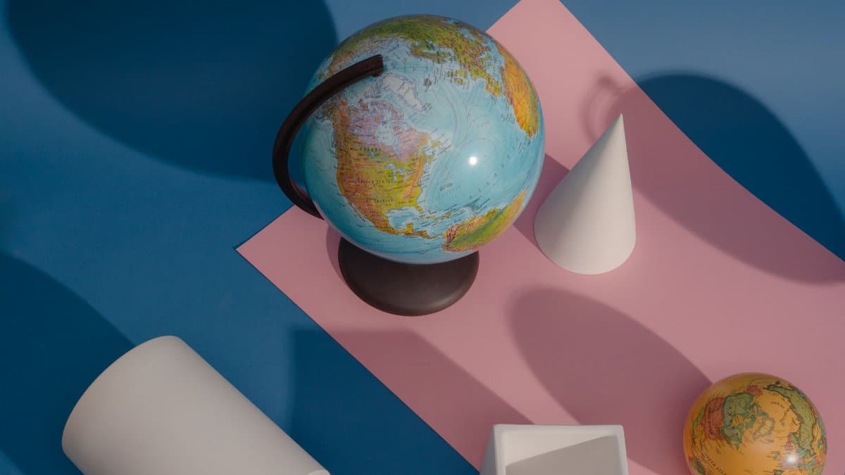 A vibrant still life featuring a globe surrounded by geometric shapes on a blue and pink background.