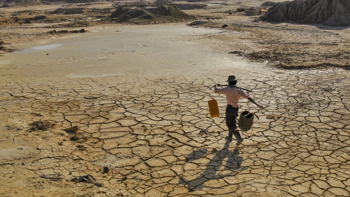 A man carries water across a parched landscape in Sagaing, revealing drought impact.