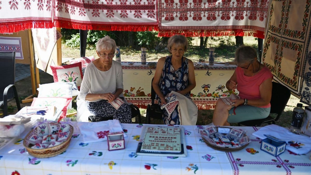 Three women showcasing handmade embroidery at a vibrant outdoor market stall.